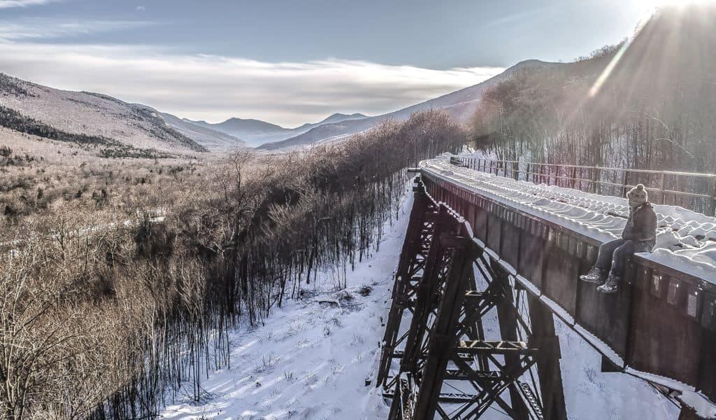 A tourist overlooks a snowy scene while sitting on a disused bridge