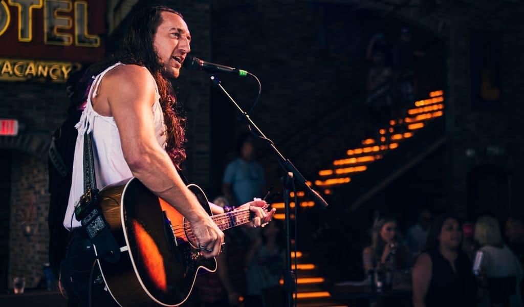 Rock country singer stands at microphone, strums guitar, while on stage in Tennessee