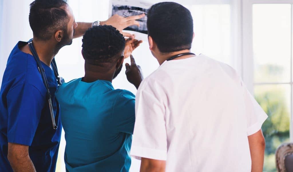 Three doctors wearing blue and white examining and discussing an X-Ray in a hospital