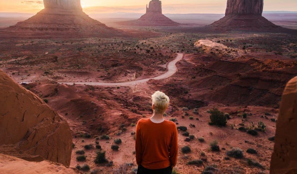 Woman wearing red shirt and black pants standing on rock overlooking the Grand Canyon