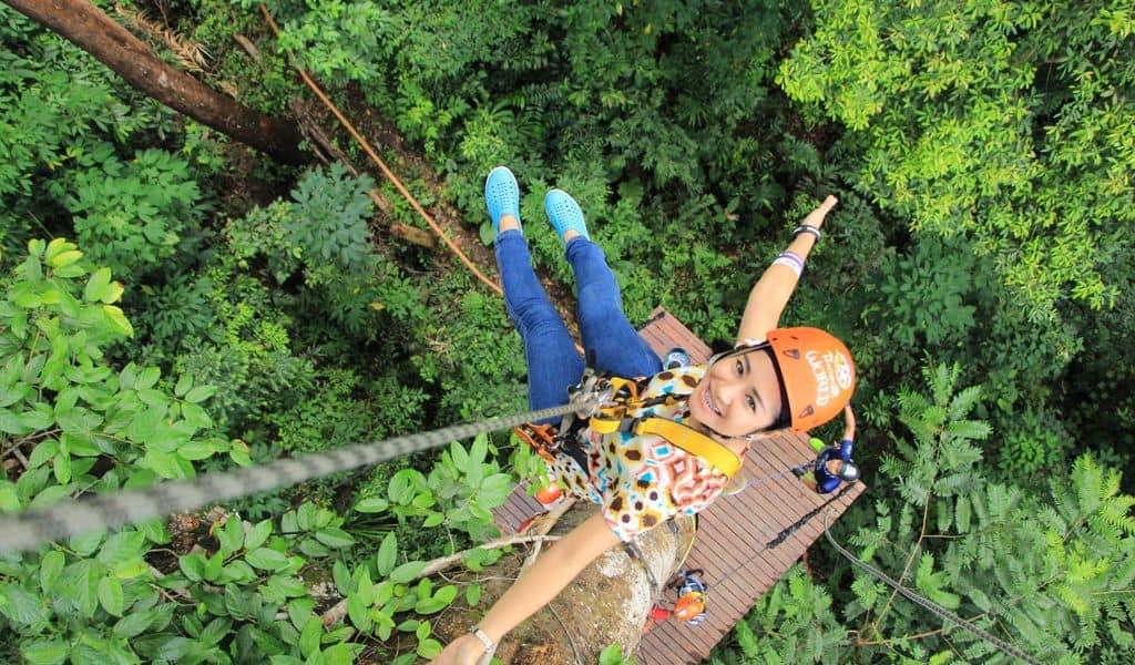 Woman wearing orange helmet strapped into ziplining equipment over a luscious forest.