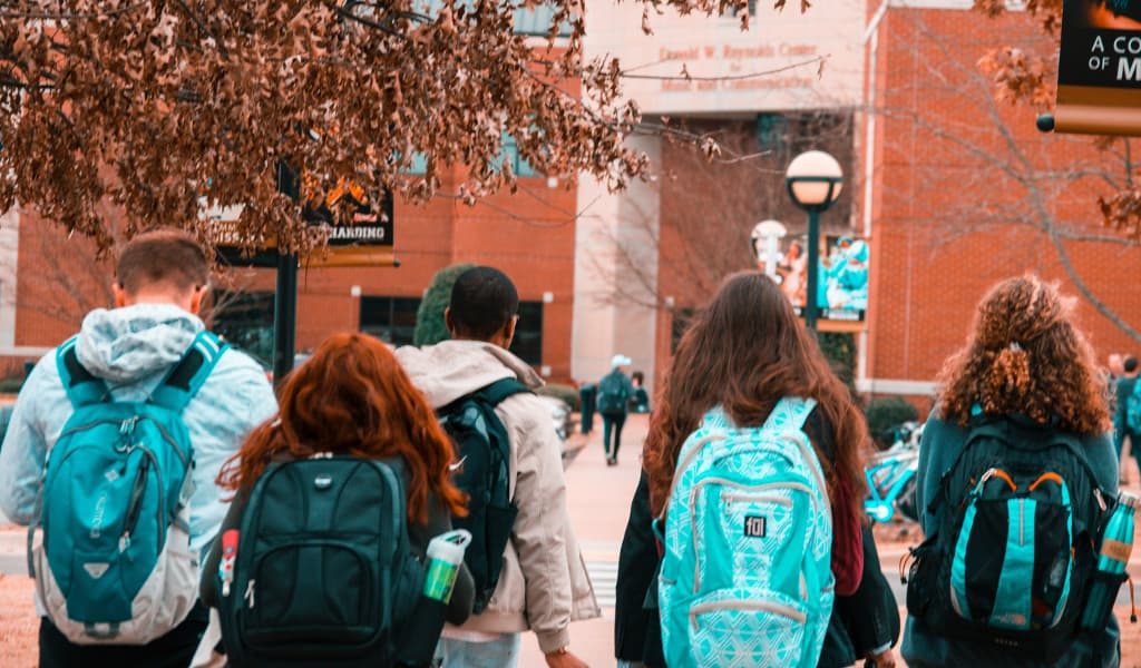 Five college students wearing backpacks with their backs facing the camera