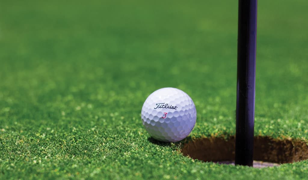 White golf ball beside hole on green grass