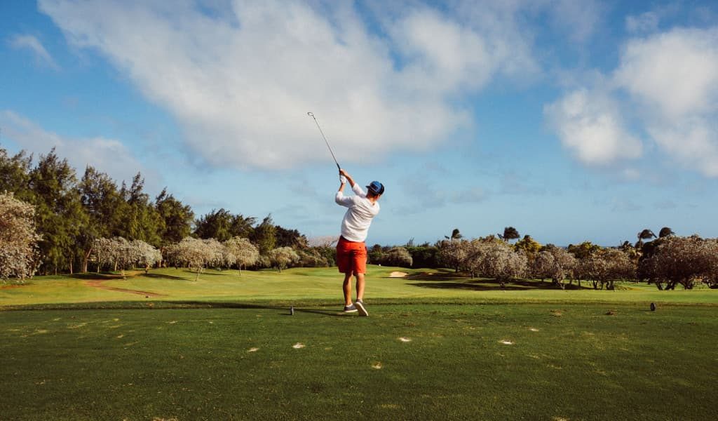 Man wearing white shirt swinging golf club on a green, luscious golf course