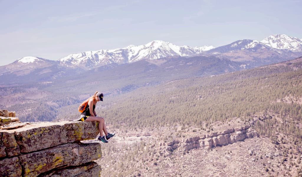 Female hiker sitting on a ledge overlooking the valley with mountains in the background