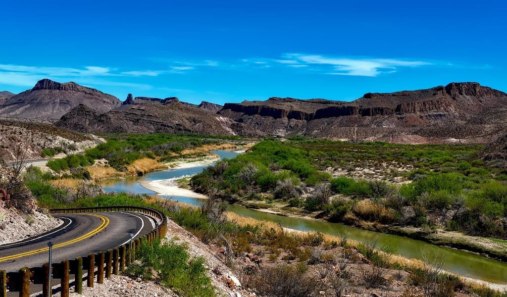 Winding road beside river with mountain and blue skies in the background