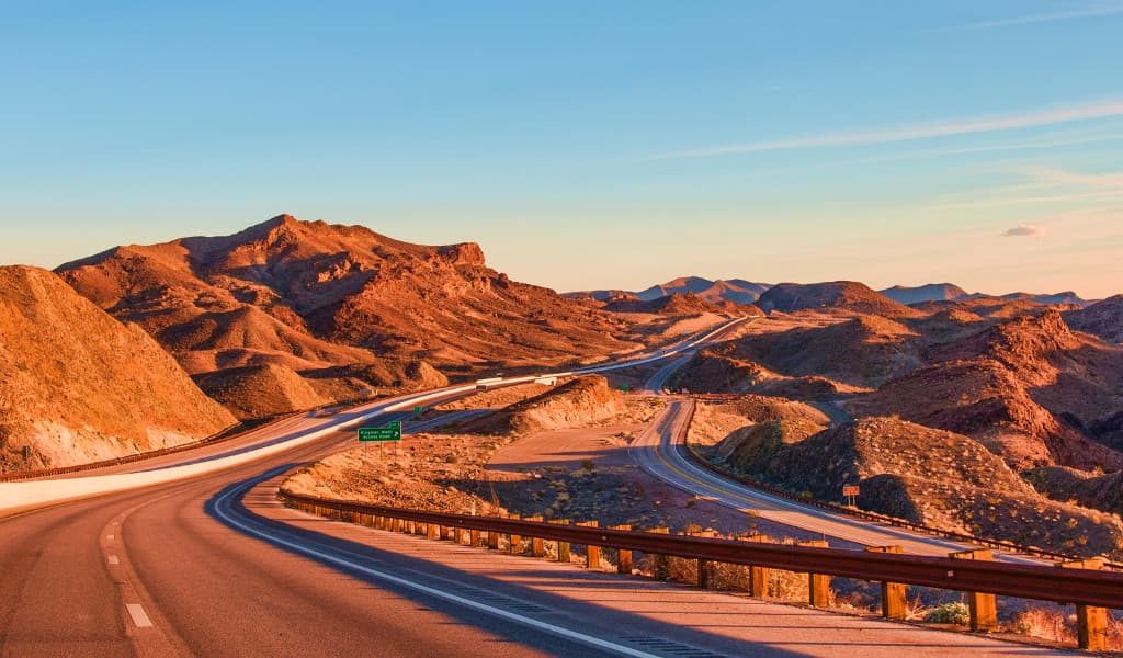 Highway road between the desert landscape and mountains below blue skies