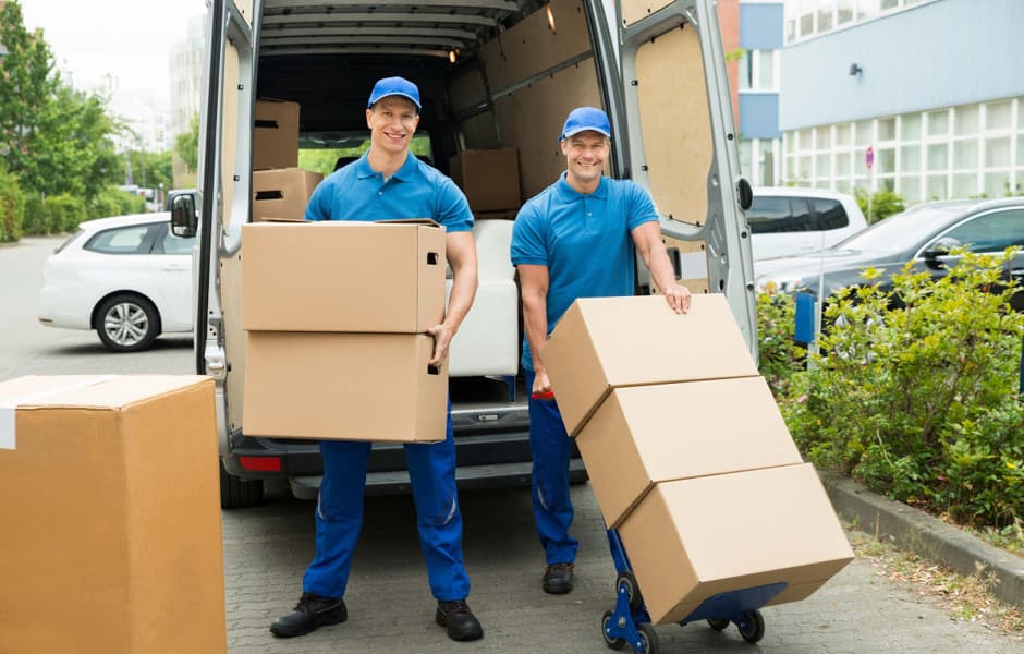 Professional movers in blue uniforms carrying a couch into a van