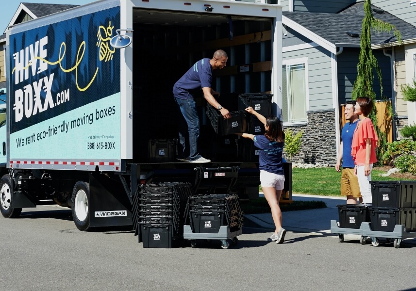 Two movers load up a truck, while the homeowners watch excitedly.