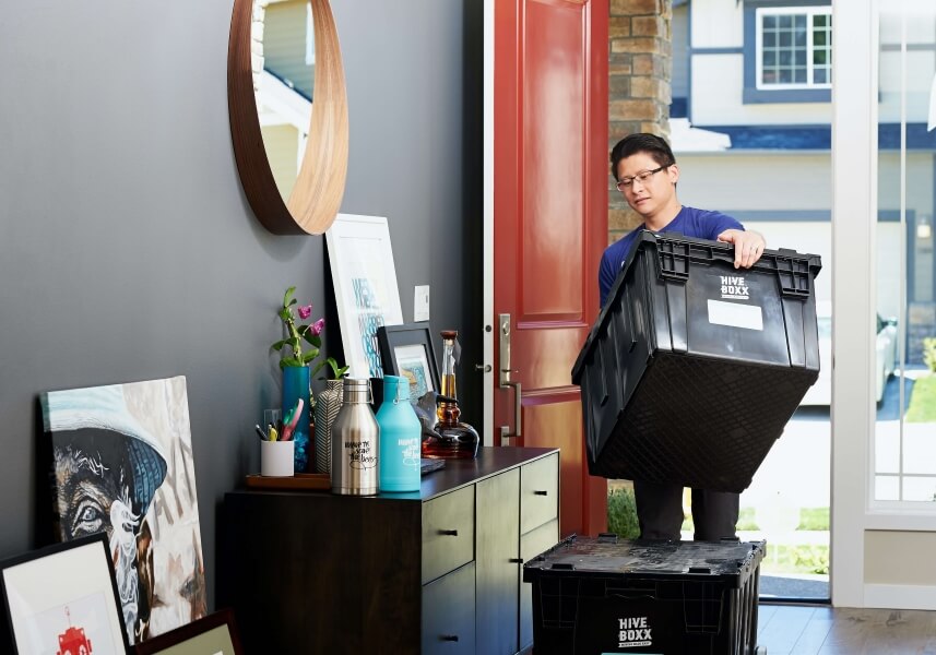 Man carries moving box into his home.