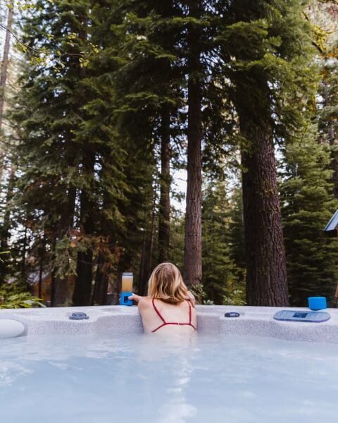 Woman relaxing with a chilled beverage in a hot tub in the woods